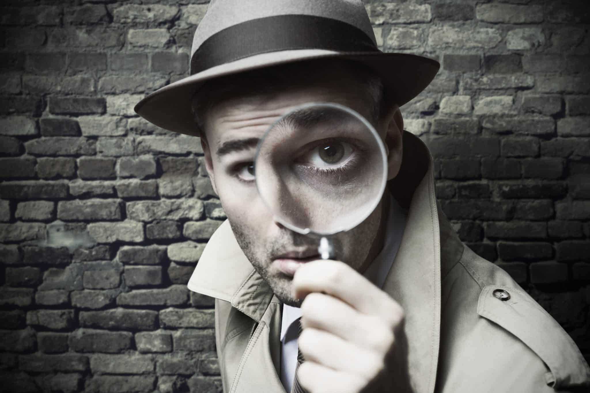 Détective en trench et chapeau scrutant un indice, ambiance escape game Laeris à Toulon.