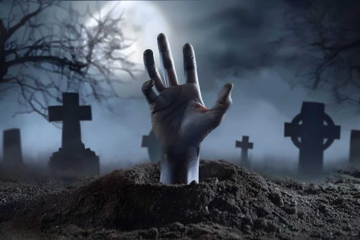 Une main sort d'une tombe, cimetière brumeux la nuit, arbres nus et pierres sous ciel nuageux.