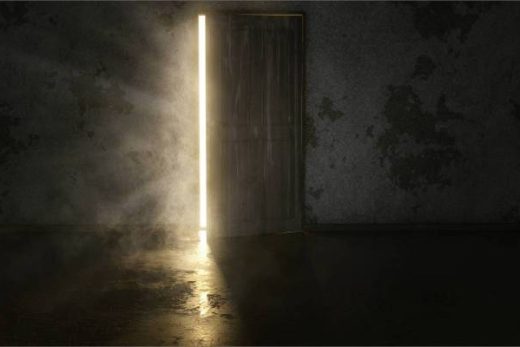 Porte entrouverte, lumière vive perçue dans pièce sombre façon escape game Laeris Toulon, murs usés.