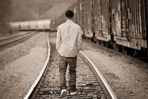 Personnage solitaire sur les rails d'un train de marchandises au ralenti, s'éloignant ; expérience immersive dans une salle d'évasion à proximité.