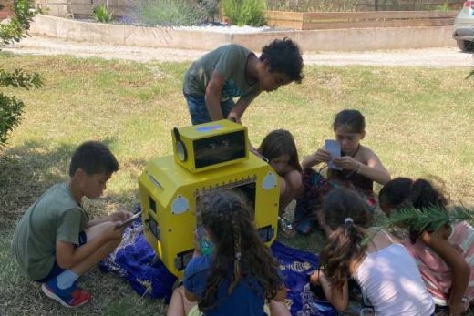Enfants réunis dehors autour d'une boîte jaune, jouant ensemble sous le soleil.