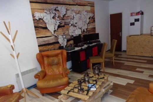 Espace chaleureux avec fauteuils, table bois, ordinateurs et déco carte du monde sur mur boisé.
