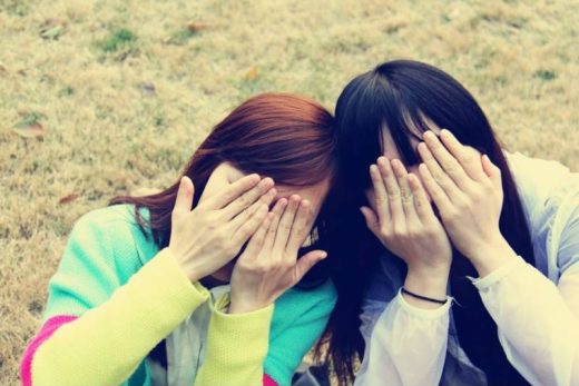 Deux personnes assises, visages cachés, têtes rapprochées, mains couvrant leur visage sur l'herbe.