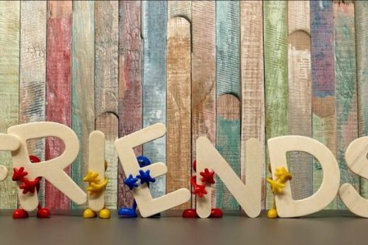Figurines colorées soulèvent les lettres "FRIENDS" devant un fond bois multicolore, ambiance conviviale.
