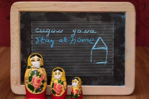 Trois matriochkas masquées devant un tableau "stay at home" et dessin de maison, ambiance jeu immersif.