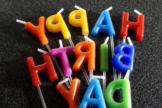 Bougies lettres multicolores "HAPPY BIRTHDAY" à l'envers, posées sur un fond sombre.