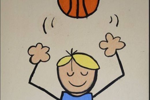 Un enfant blond souriant, vêtu d'une chemise bleue et d'un short vert, lance un ballon de basket orange au-dessus de sa tête.