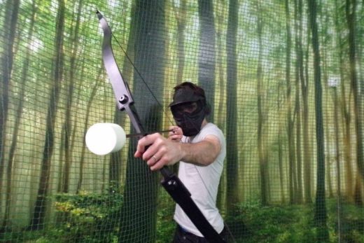 Joueur masqué vise à l'arc mousse, décor forêt immersif, ambiance escape game Laeris Toulon.