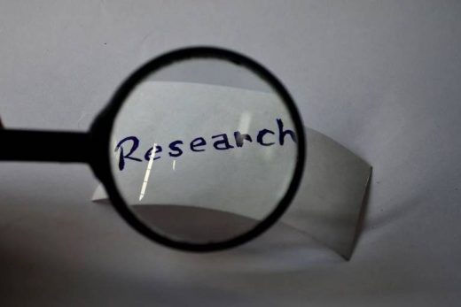 Une loupe agrandit "Research" écrit à la main sur papier, ambiance épurée et mystérieuse.