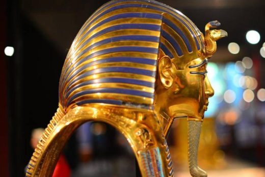 Masque de pharaon doré aux accents bleus, vue latérale, présenté dans un musée iconique, une expérience immersive vous attend.