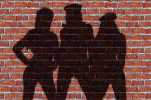 Silhouettes de trois joueurs chapeautés sur un mur en briques rouges, ambiance escape game immersive.
