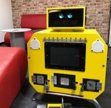 Robot jaune à écran, boutons, yeux ronds près d'un canapé rouge et d'une boîte à outils noire.
