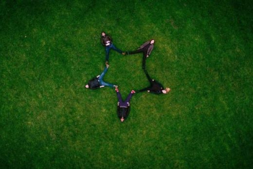 Vue du ciel de 6 joueurs formant une étoile en cercle sur l'herbe, pieds réunis au centre.