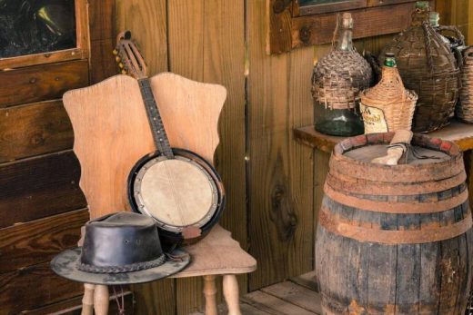 Banjo et chapeau sur chaise, tonneau rustique et bouteilles, ambiance vintage bois.
