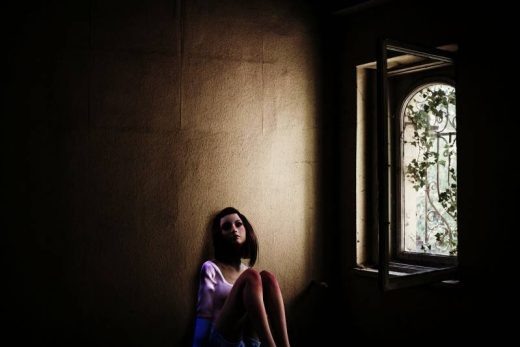 Femme assise au sol, mur sombre, près fenêtre ouverte avec lierre dehors. Atmosphère immersive et mystérieuse.