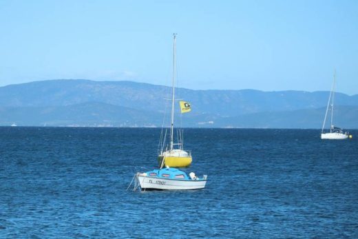 Voilier blanc, annexe jaune et drapeau sur mer bleue, montagnes lointaines, ambiance détente Toulon.
