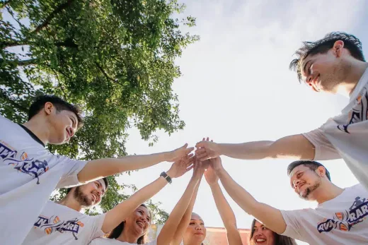 Six personnes cercle extérieur, mains jointes, t-shirts "Run Rare", ciel et arbres en arrière-plan.