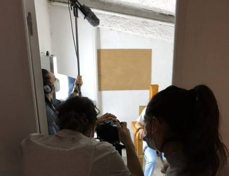 Équipe filme une personne assise dans une pièce, caméra et perche micro, immersion totale.