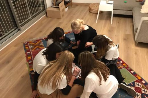 Groupe de femmes en cercle, concentration sur un objet au centre, salon épuré, ambiance conviviale.