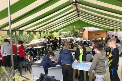 Ateliers en groupe sous tente rayée, ambiance ludique et organisée avec tables et chaises alignées.