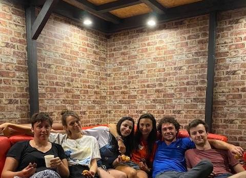 Groupe de six personnes sur canapé rouge, ambiance chaleureuse, parfait pour team building ou anniversaire.