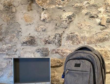 Sac gris et mallette d'équipement sur table en bois, ambiance escape game toulonnais authentique.