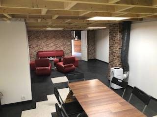 Salle de réunion design : table bois, chaises noires, canapés rouges, briques et poutres apparentes.