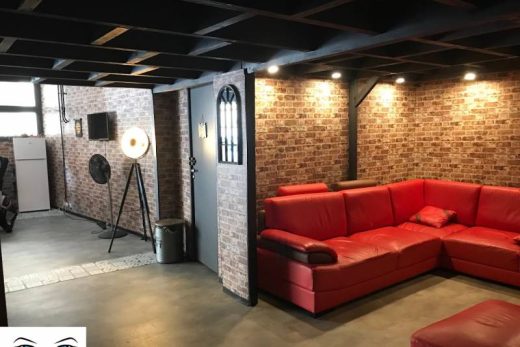 Salon chaleureux, canapé rouge, murs en briques, poutres apparentes et logo Laberinto Escape distinctif.