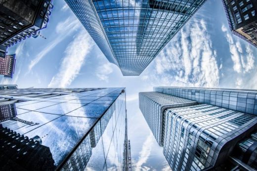 Gratte-ciels toulonnais, reflets nuageux sur façades vitrées, immersion urbaine vers le ciel bleu.
