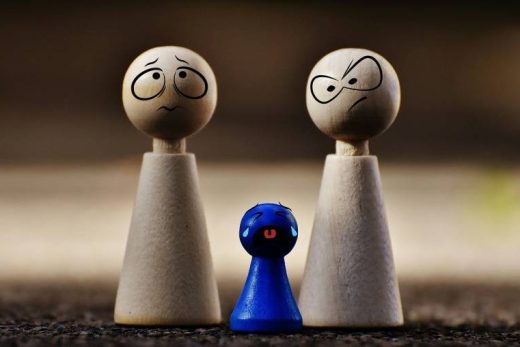 Deux figurines bois inquiètes et fâchées à côté d'une petite bleue triste, en pleurs.