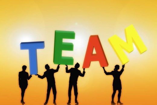 Quatre personnes silhouette soulèvent les lettres colorées "TEAM" sur fond jaune, ambiance team building.
