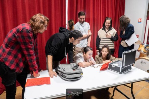 Joueurs autour d'une table, accessoires d'escape game ; rideaux rouges en fond, ambiance immersive.