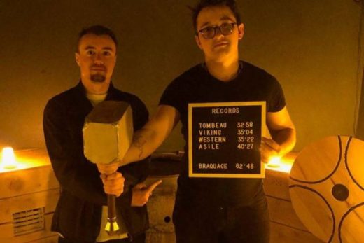 Deux joueurs posent, marteau d'accessoire et panneau avec scores des rooms Laeris en main.