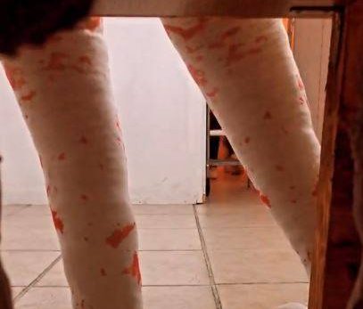 Deux jambes bandées blanc à pois orange, sous table, sol carrelé.