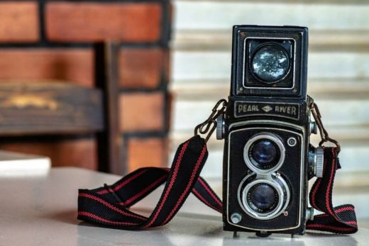 Appareil photo vintage Pearl River sur fond flou, avec sangle noire et rouge posé sur surface blanche.