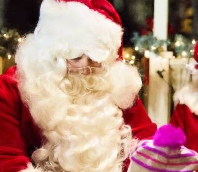 Père Noël en rouge et enfant joyeux, bonnet coloré, moment festif lors d'un événement hivernal extérieur.