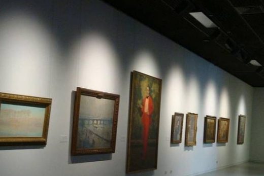 Galerie d'art, éclairage tamisé, mur blanc, tableaux encadrés, centre de table avec un portrait rouge saisissant.