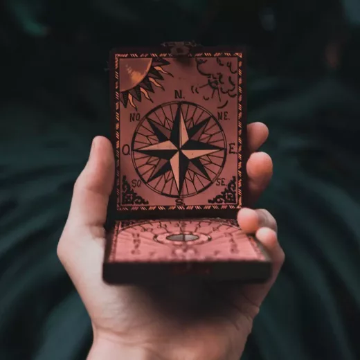 Boîte en bois ouverte avec boussole décorative, tenue à la main devant un fond neutre.