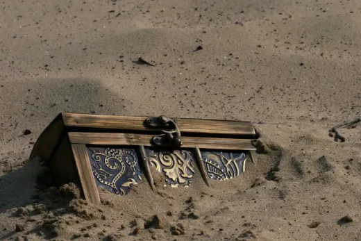 Coffre en bois orné, partiellement enfoui dans le sable, prêt à révéler ses secrets d'escape game.