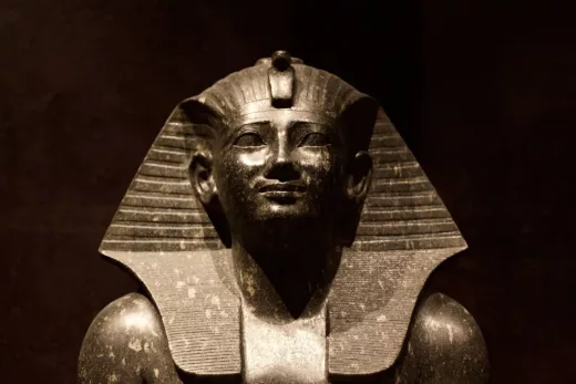 Statue égyptienne pharaon, coiffe nemes, pierre lumineuse sur fond sombre.