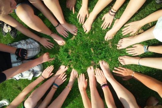 Cercle de joueurs assis sur l'herbe, mains et pieds nus tendus vers le centre.