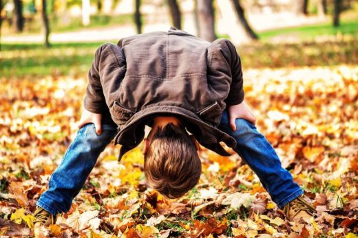 Enfant penché, regarde à travers ses jambes sur des feuilles d'automne, dans un parc arboré.