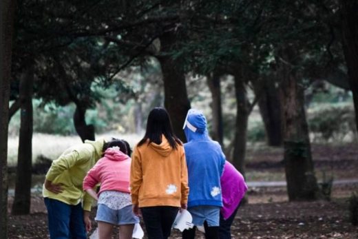 Joueurs en sweat colorés cherchent des indices dans la forêt, plongés en plein escape game immersif.