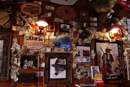 Mur de bar orné de photos, affiches et billets décorant des panneaux bois dans une ambiance conviviale.