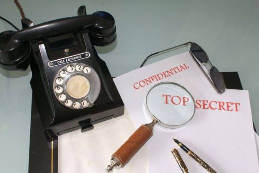 Objets d'enquête sur un bureau : téléphone, loupe, stylos, lunettes et dossiers "Confidentiel", "Top Secret".