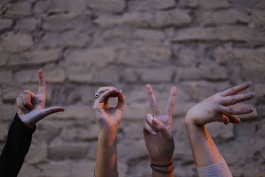 Quatre mains forment "LOVE" en langue des signes devant un mur de briques flou.